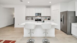 A modern kitchen with white cabinetry, a stainless steel refrigerator, and two bar stools.