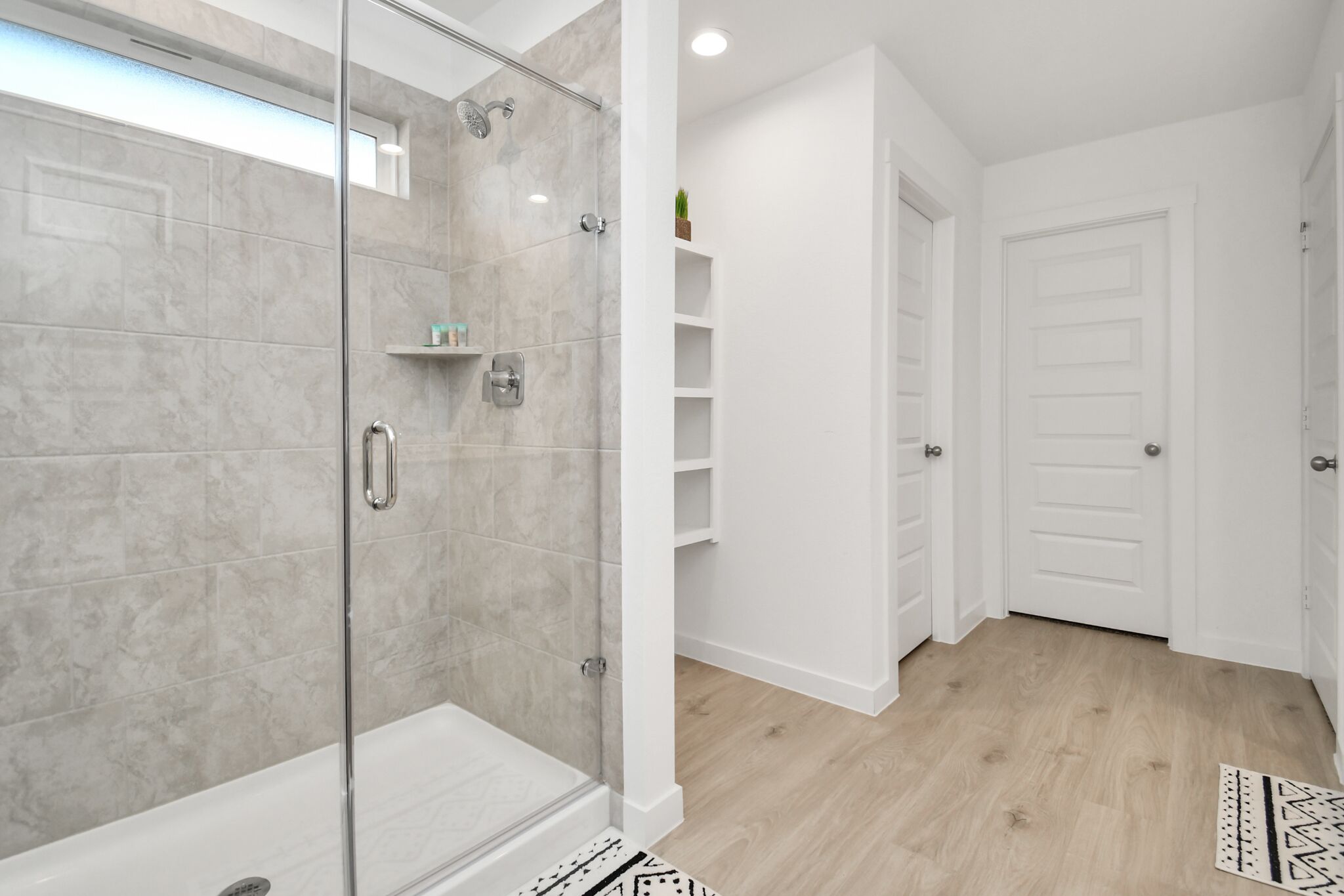 Een moderne badkamer met een douche met glazen wand, witte betegelde muren en een houten vloer.