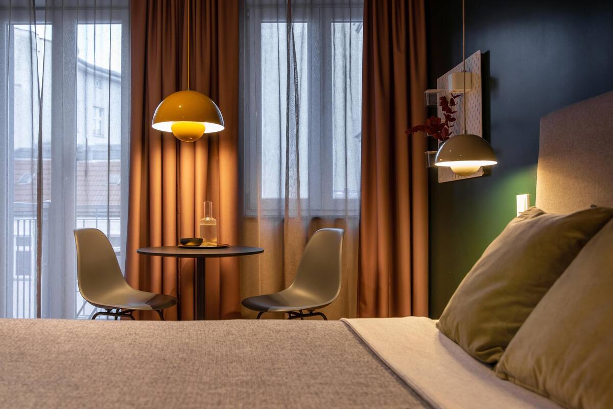 A hotel room with a bed, two chairs, a small table, and two pendant lights.