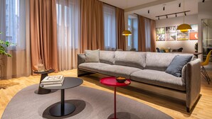 A modern living room with a sofa, a coffee table, a red side table, and a bookshelf. - ipartment Berlin Mitte @HOME by Best Western (Berlin)