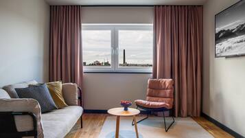 A modern living room with a sofa, a chair, a small table with a bowl of fruit, and a window with a cityscape view.