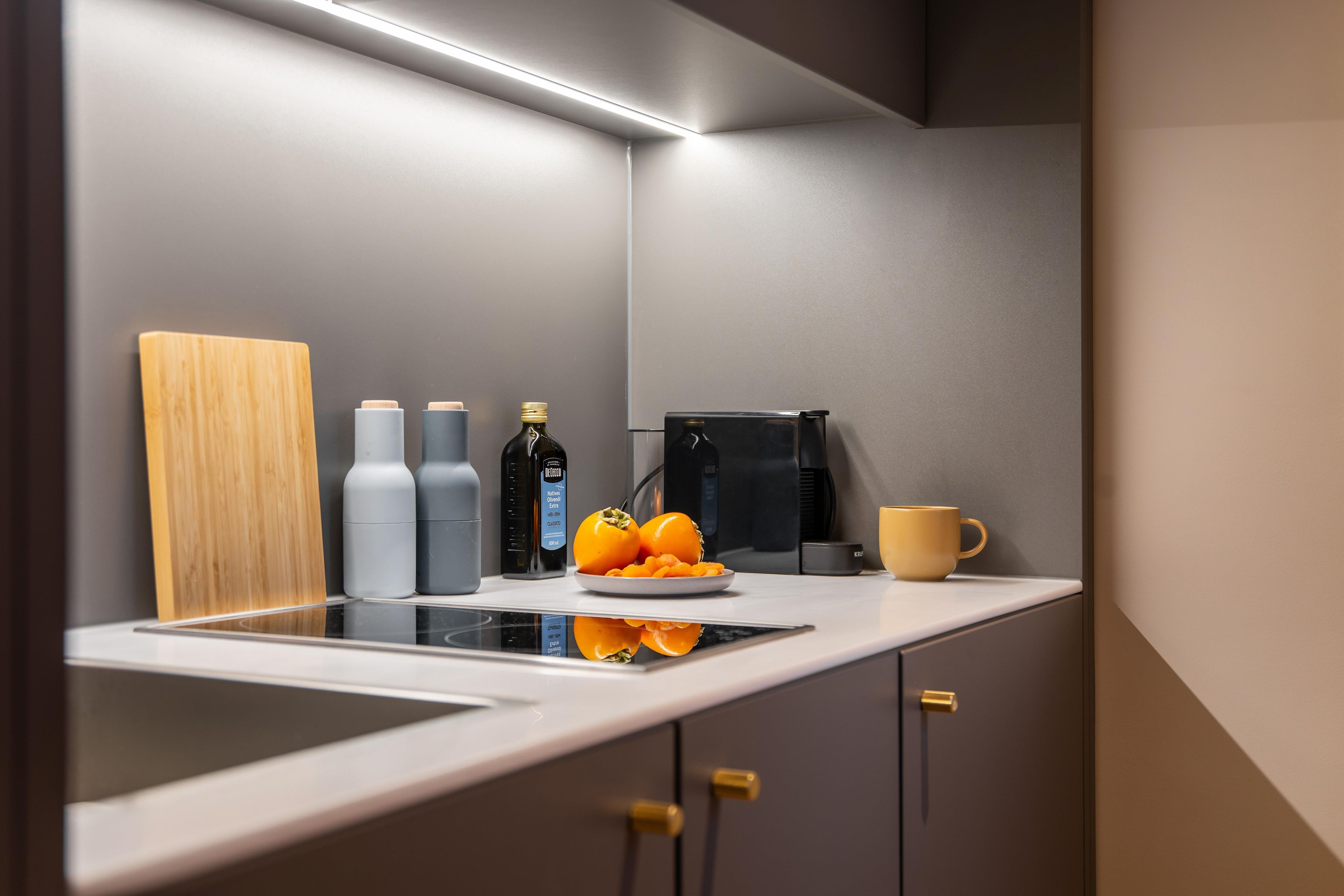 A modern kitchen with a built-in stove, a coffee maker, and a bowl of fruit on the counter.