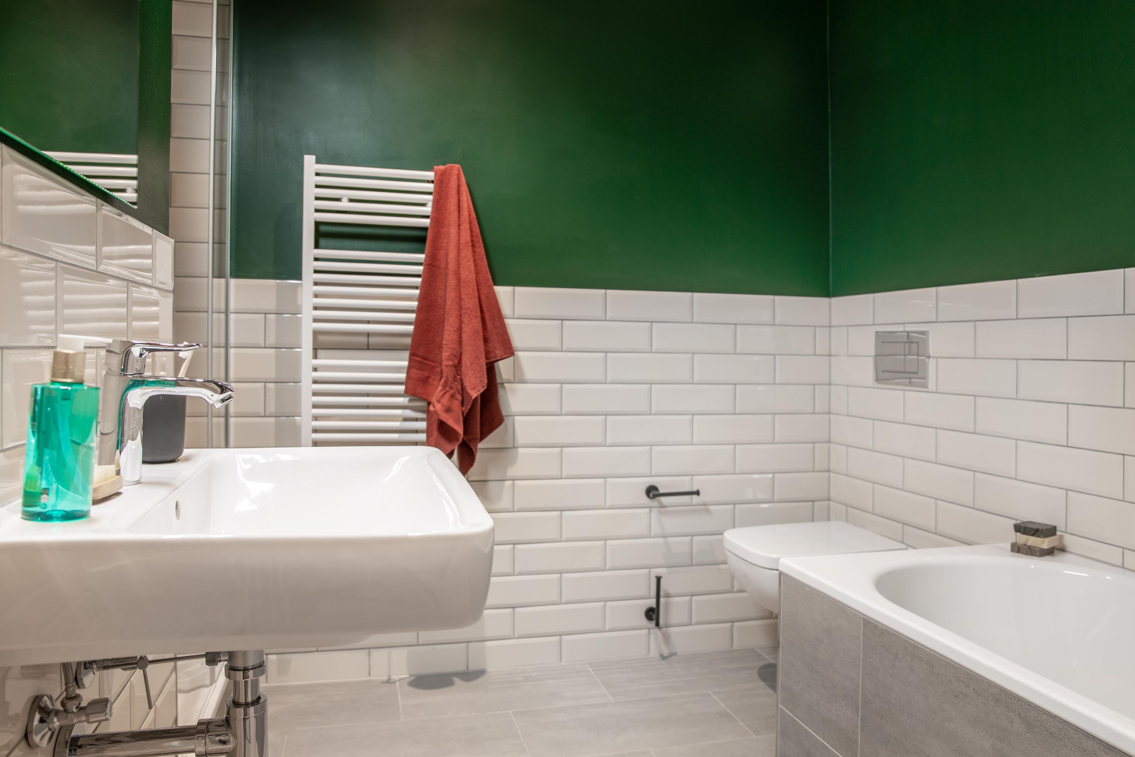 A bathroom with a white sink, a mirror, a green wall, and a white bathtub.