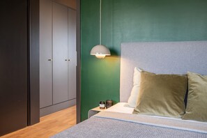 A bedroom with a bed, pillows, a nightstand, a lamp, and a wardrobe.
