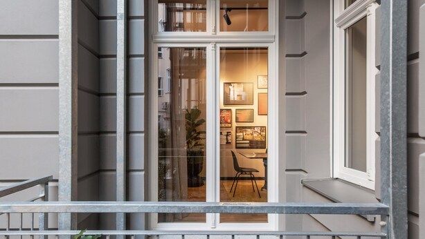 A building with a balcony, a door with glass panels, and a visible interior with a chair and framed pictures. - ipartment Berlin Mitte @HOME by Best Western (Berlin)