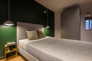 A neatly made bed with a grey headboard and two pillows, a bedside table with a lamp, and a wardrobe with a mirror. - ipartment Berlin Mitte @HOME by Best Western (Berlin)