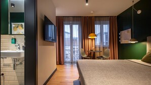 A hotel room with a bed, a desk, a chair, a TV, and a bathroom with a sink and mirror. - ipartment Berlin Mitte @HOME by Best Western (Berlin)