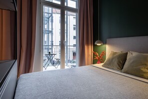 Habitación de hotel con cama, cortinas, vistas al exterior y una pequeña mesa con sillas.