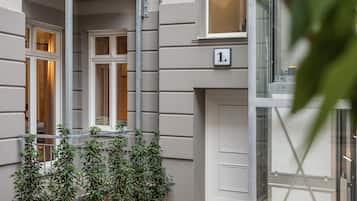 A building facade with a numbered door, a window, and a small garden area with plants.