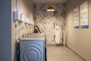 A laundry facility with multiple washing machines, a drying station, and instructional posters on the wall.