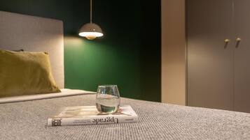 A glass of water on a magazine on a textured carpet, a hanging light, a green wall, and a bed with a yellow pillow.