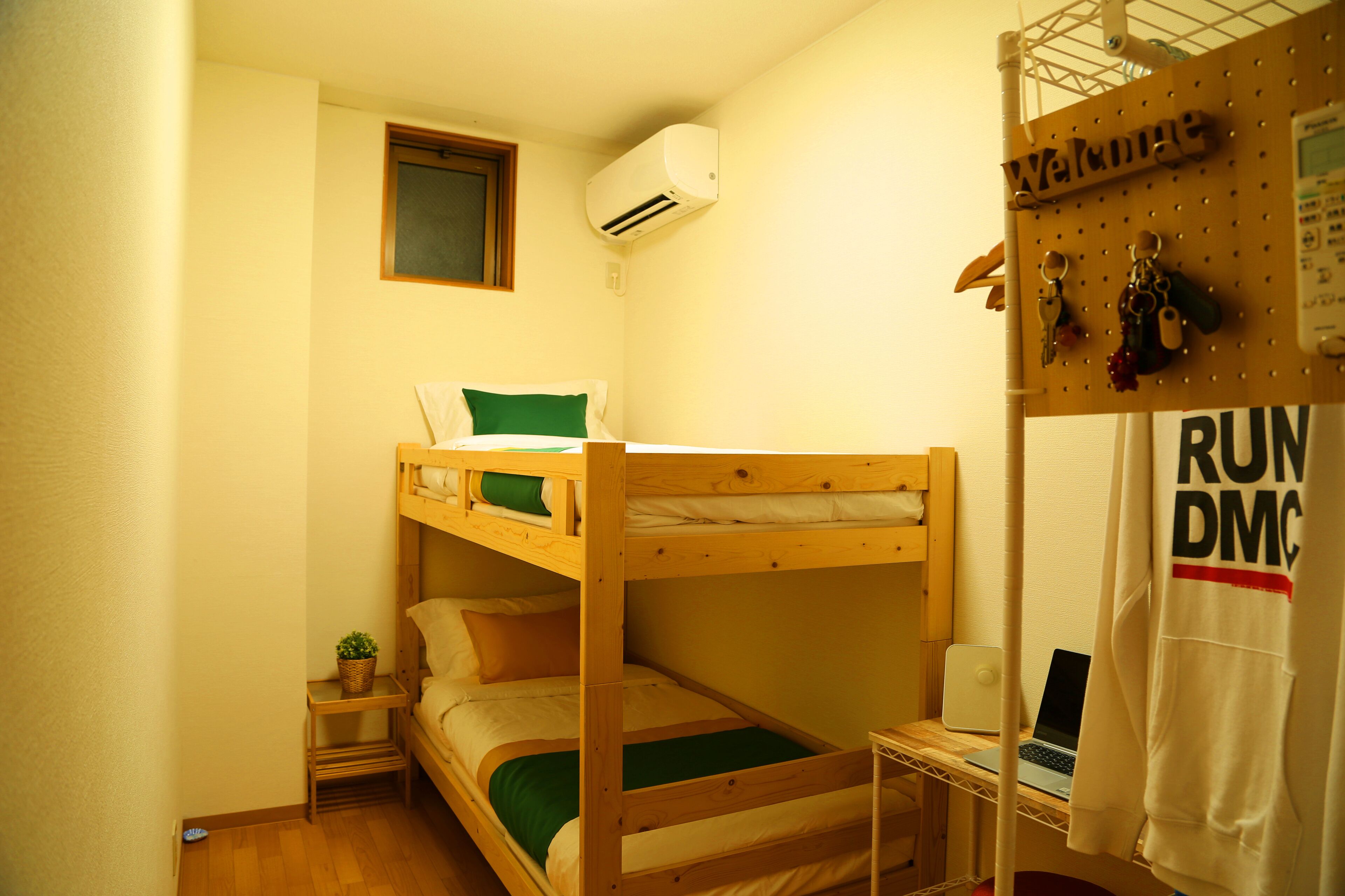 A bunk bed room with a small table, a wall-mounted air conditioner, and a welcome sign.