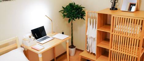 A bedroom with a wooden desk, a laptop, a potted plant, a mirror, and a shoe rack.