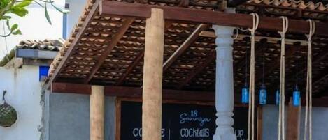 Two people sitting at a wooden table with a drink and a menu in a covered outdoor area with columns and a hanging light fixture.