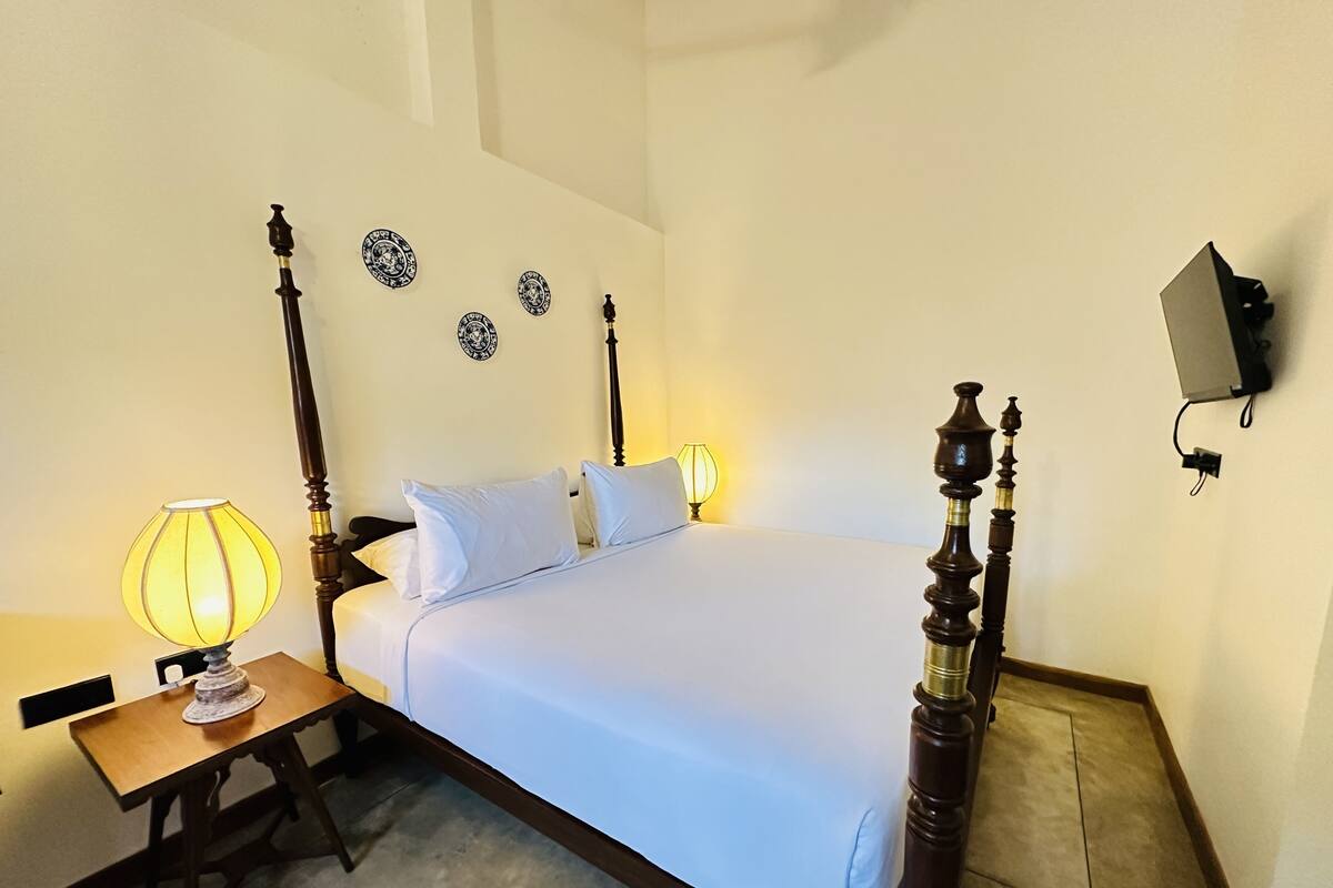 Een keurig opgemaakt bed met witte lakens, een houten hoofdbord en een nachtkastje met een lamp.