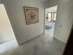 Un pasillo con piso de baldosas que lleva a un dormitorio con cama y una silla roja.