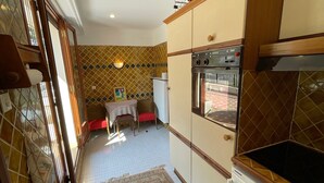 Une cuisine compacte dotée d’un four encastré, un coin repas avec une table et des chaises, et un mur orné d’un motif décoratif.