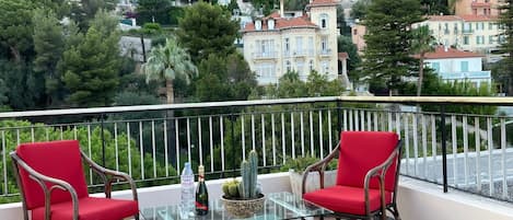 A balcony with two red chairs, a glass table, and a bottle of Evian water.
