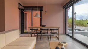 Un interno moderno con un divano, un tavolo da pranzo con sedie, una lampada a sospensione e una vista panoramica attraverso ampie finestre.
