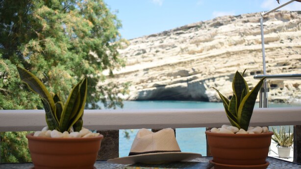 A balcony with terracotta pots containing green plants, a hat, and a colorful book. - Seaside Nicola's Studio (Matala)