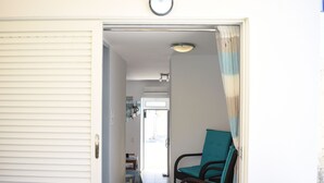 A hallway with a closed door, a chair with a teal cushion, and a tiled floor. - Seaside Nicola's Studio (Matala)