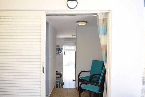 Un couloir avec une porte fermée, une chaise dotée d’un coussin de couleur turquoise et un sol carrelé.