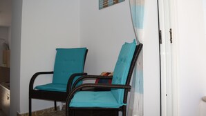 Two wicker chairs with teal cushions in a room with white walls and a door with a curtain. - Seaside Nicola's Studio (Matala)