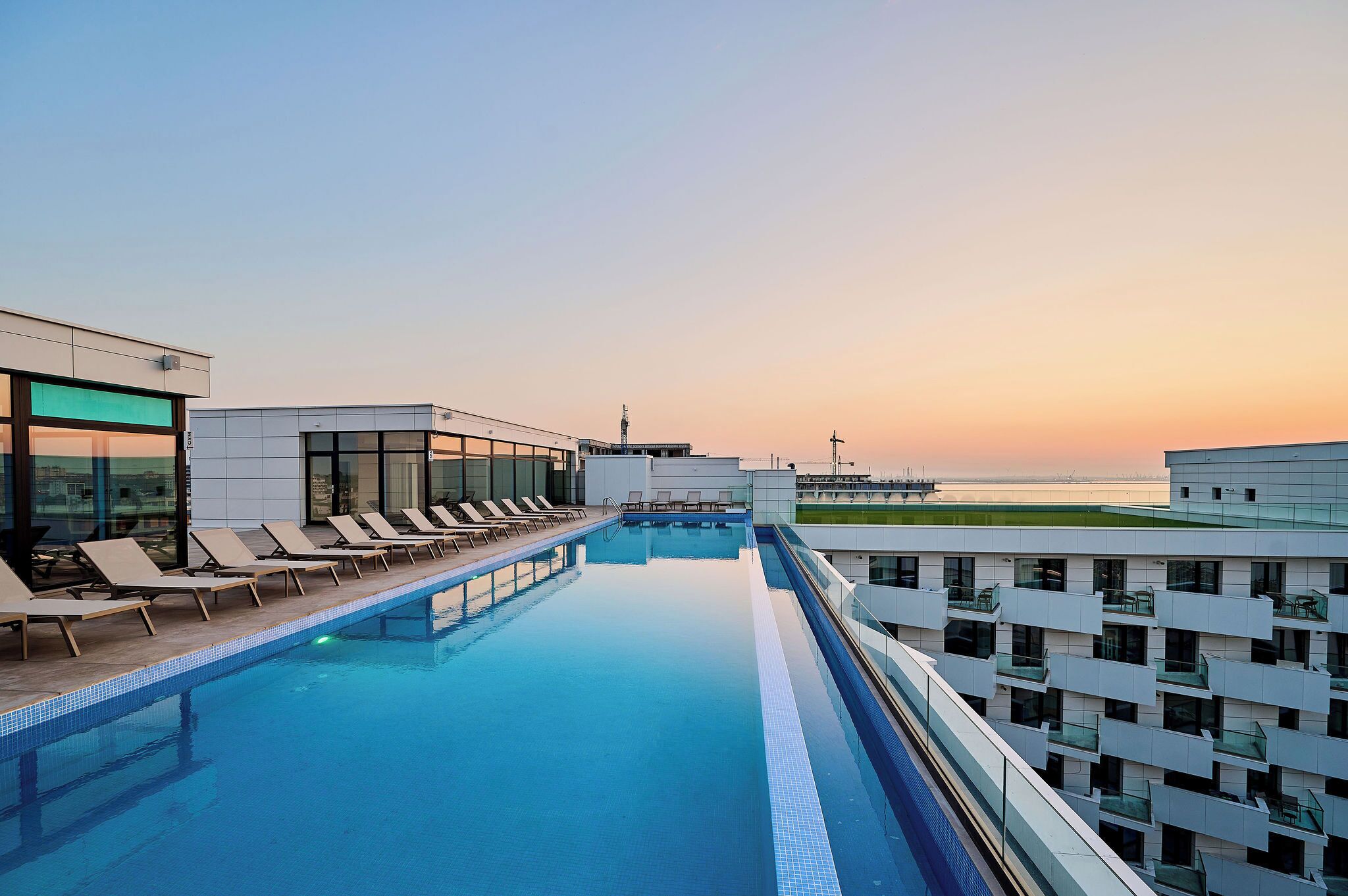 Ein Pool auf dem Dach mit Liegestühlen und Blick auf den Sonnenuntergang.