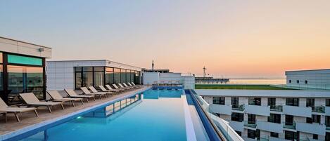Ein Pool auf dem Dach mit Liegestühlen und Blick auf den Sonnenuntergang.