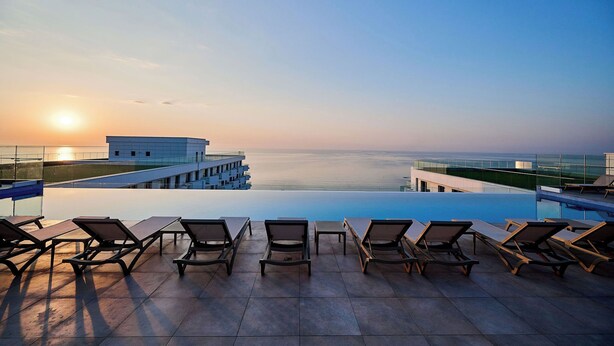 An infinity pool with lounge chairs, overlooking a body of water and a modern building. - ALEZZI INFINITY RESORT & SPA (Navodari)