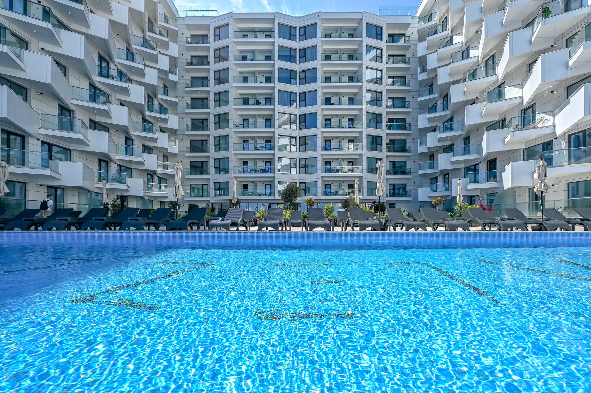 Ein modernes Hotel mit zentralem Schwimmbad, mehreren Balkonen und Liegestühlen.