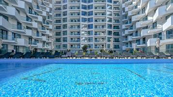 Ein modernes Hotel mit zentralem Schwimmbad, mehreren Balkonen und Liegestühlen.