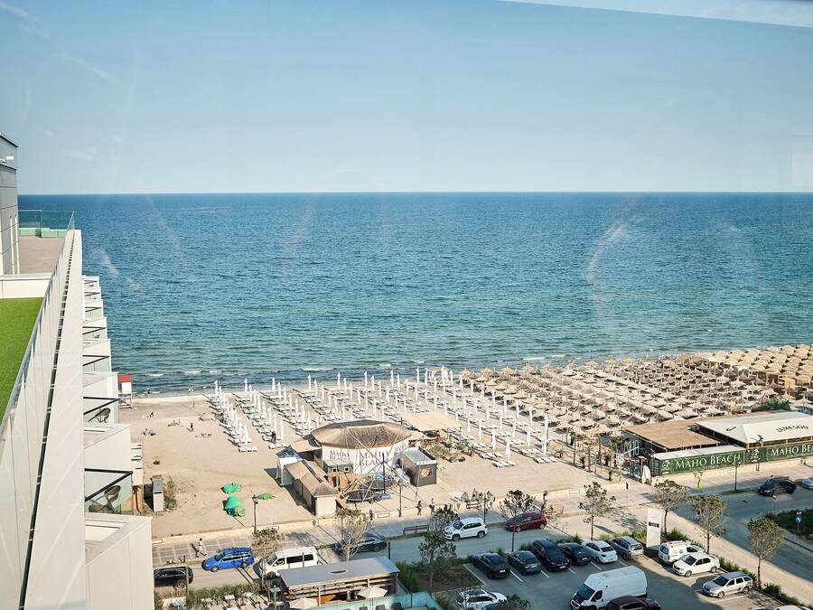Un hotel frente a la playa con un amplio espacio de piscina, una playa con sombrillas y vistas despejadas al océano.