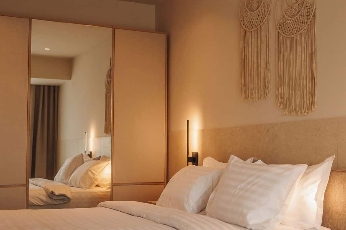 Una habitación de hotel moderna con una cama grande, un espejo, un adorno de macramé en la pared y una mesita de noche con una lámpara.