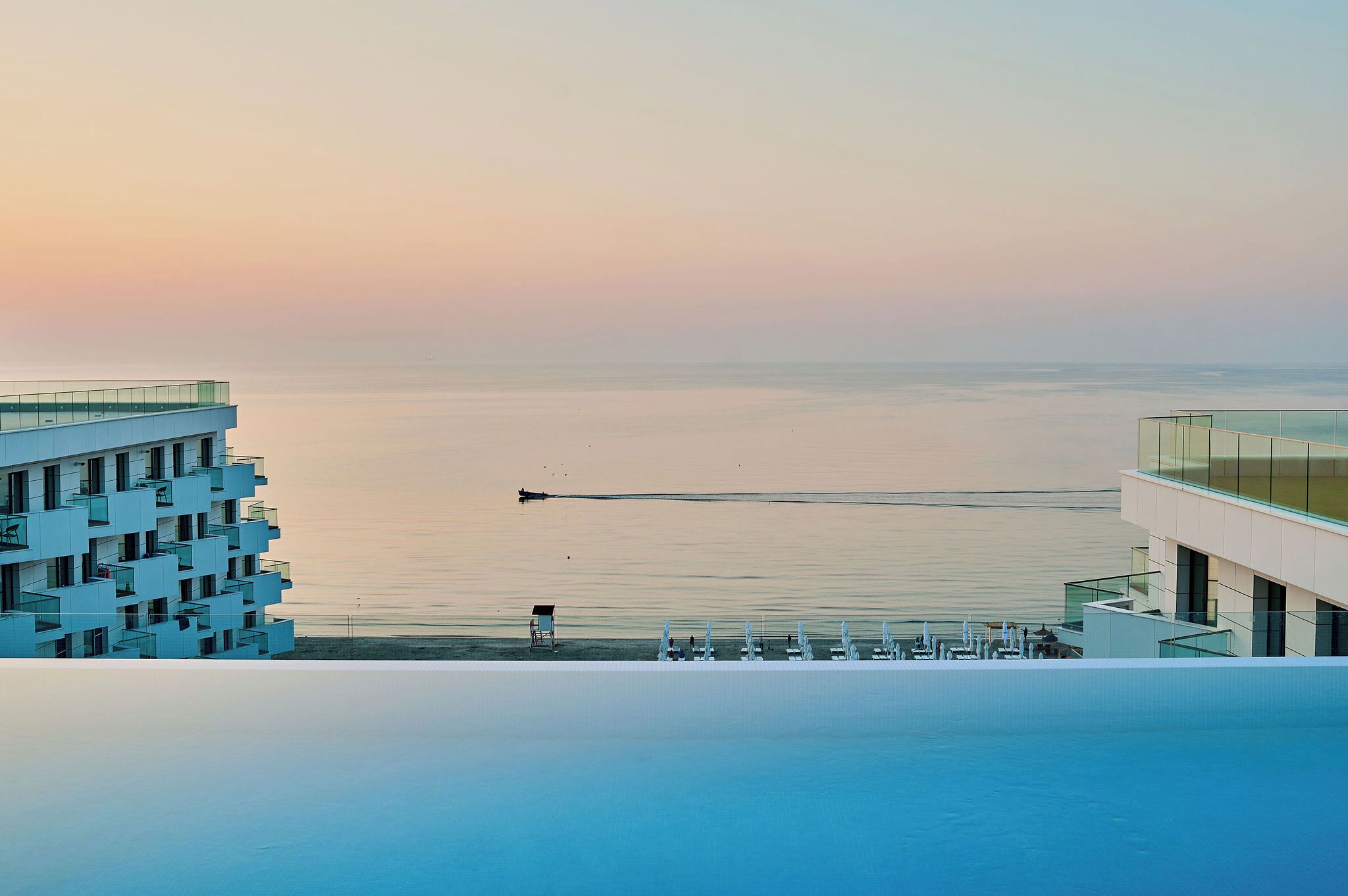 A modern building with a rooftop pool overlooking a calm sea.
