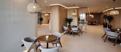 A modern hotel lobby with round tables and chairs, ambient lighting, and a wooden accent wall.