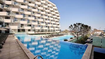 A modern hotel with a large swimming pool, multiple balconies, and a clear view of the surrounding area.