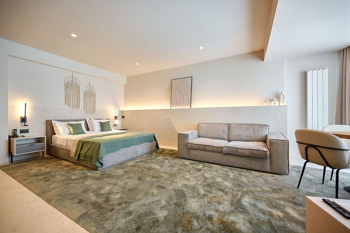 Una habitación de hotel moderna con cama, sofá, sillón y escritorio.