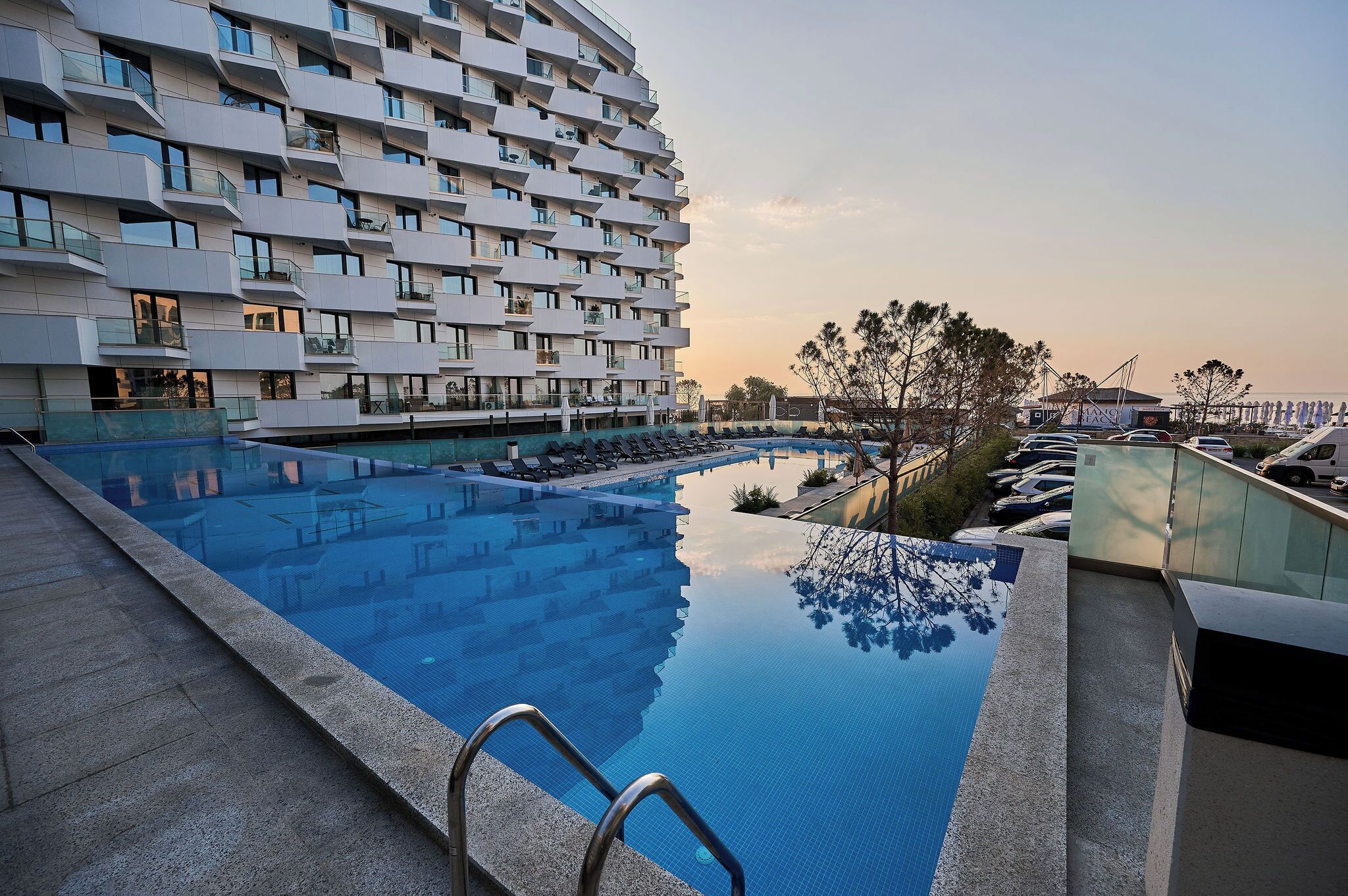 A modern hotel with a rooftop infinity pool, reflecting the building and sky.