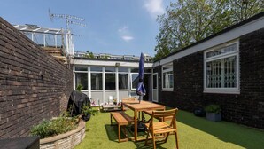 Ein Garten mit Holztisch und -stühlen, einem Grill und einem Fenster mit Blick auf den Garten.