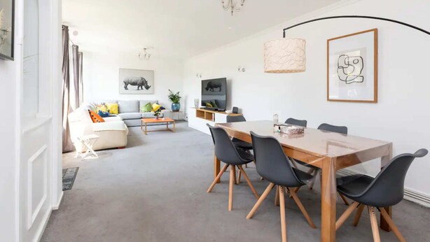 Ein modernes Wohnzimmer mit Essbereich, ausgestattet mit einem Holztisch, schwarzen Stühlen, einer Couch und einem Couchtisch.
