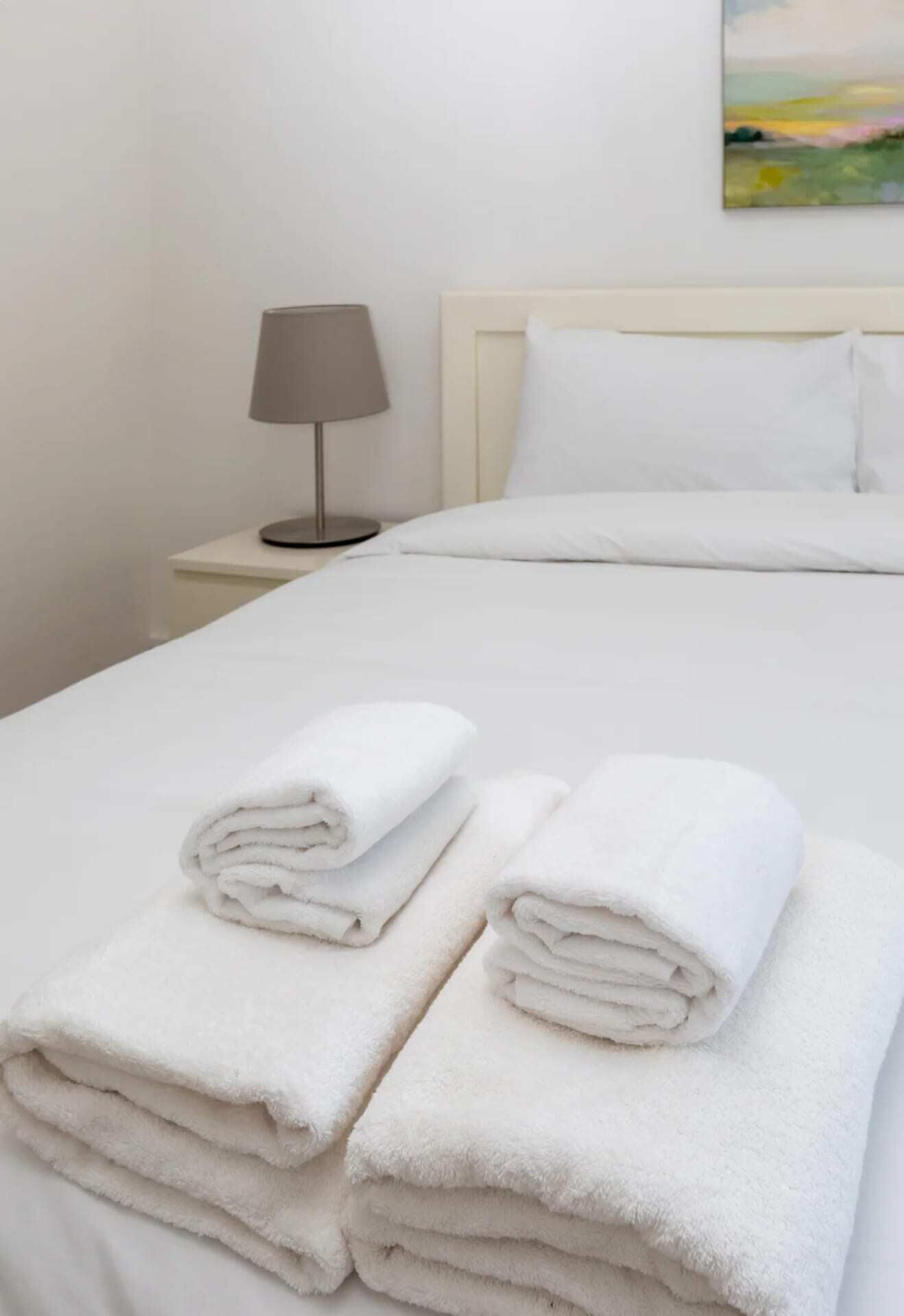 A neatly made bed with white linens and two folded towels on the bed.