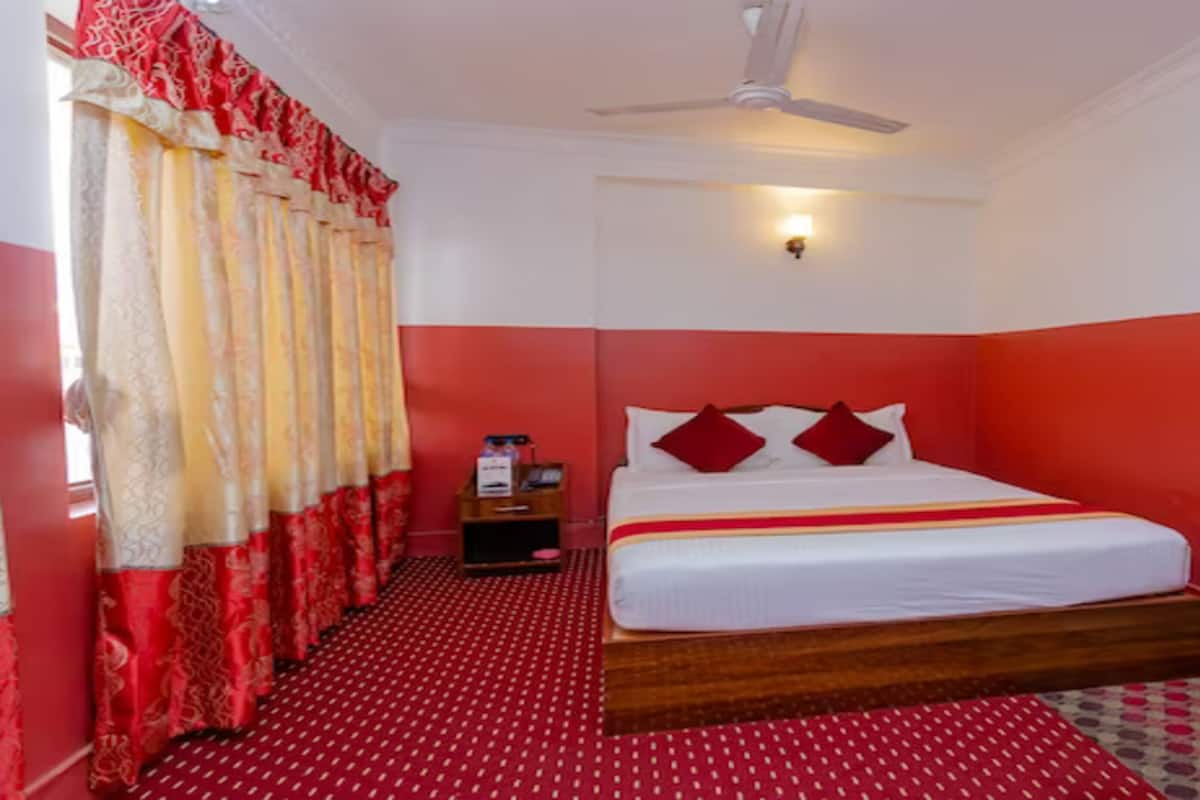 A room with a bed, a nightstand, a ceiling fan, and a window with curtains.