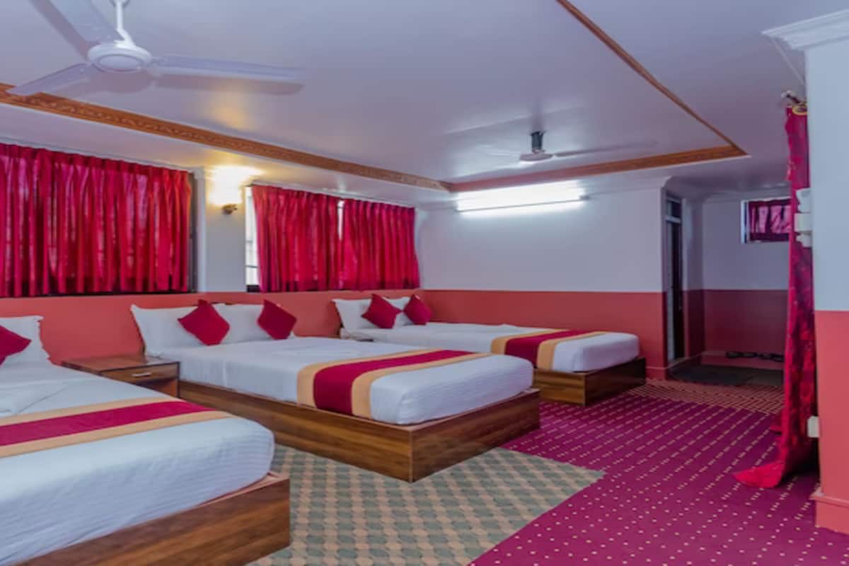 A hotel room with three beds, red curtains, a ceiling fan, and a patterned carpet.