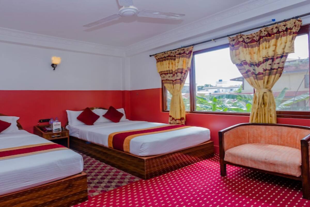A hotel room with two beds, a chair, a ceiling fan, and a window with curtains.