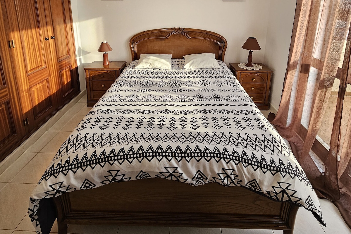 Une chambre à coucher avec un lit en bois, une table de chevet, une commode et deux tableaux encadrés au mur.