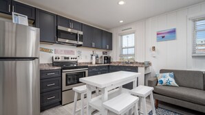 A modern kitchen with dark cabinets, stainless steel appliances, a white dining table with bar stools, and a gray sofa with a blue and white patterned throw pillow. - Two bedroom ocean block condo in a great location! (Ocean City)