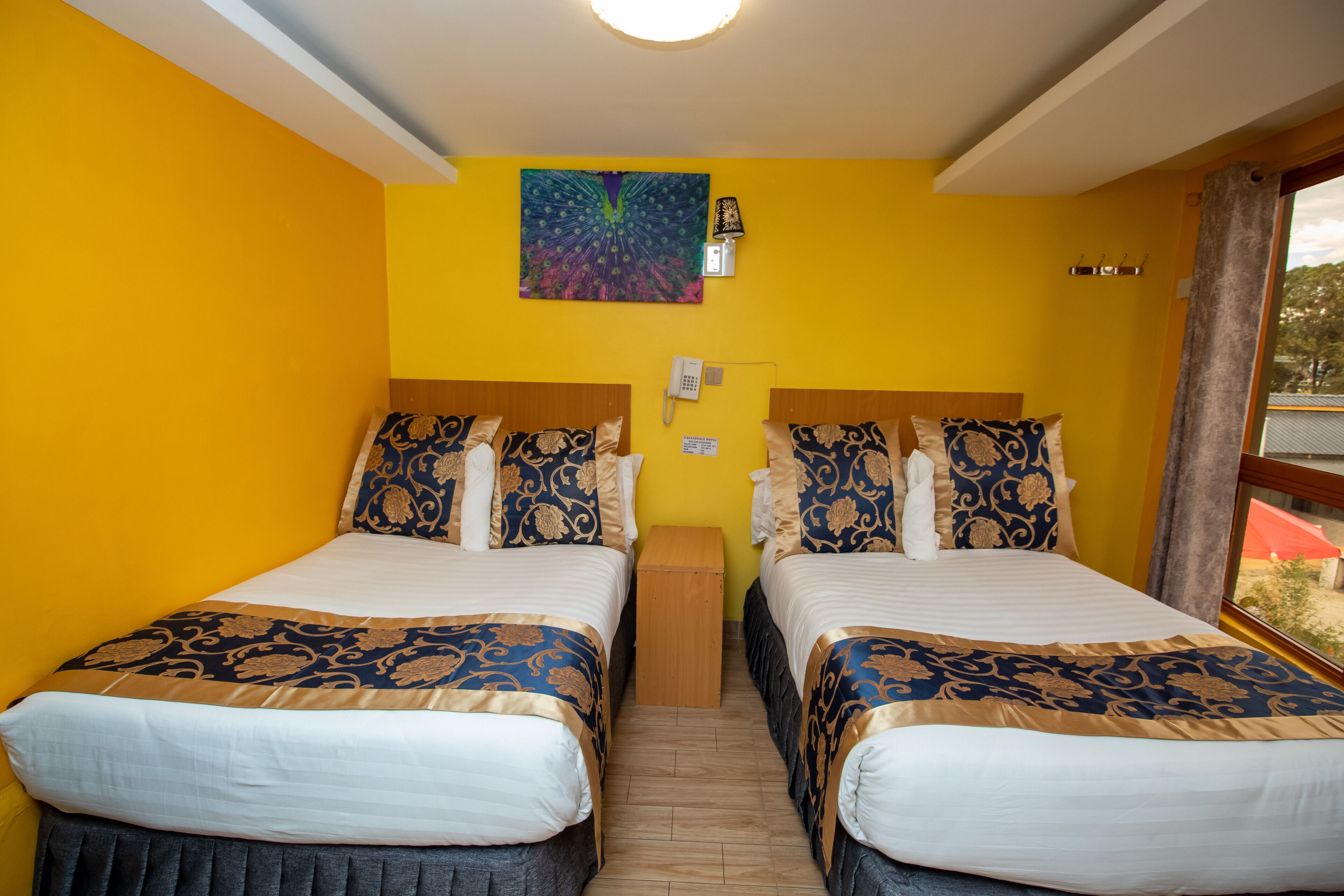 Een kamer met twee bedden, een houten nachtkastje, een telefoon en een kleurrijk kunstwerk aan de muur.