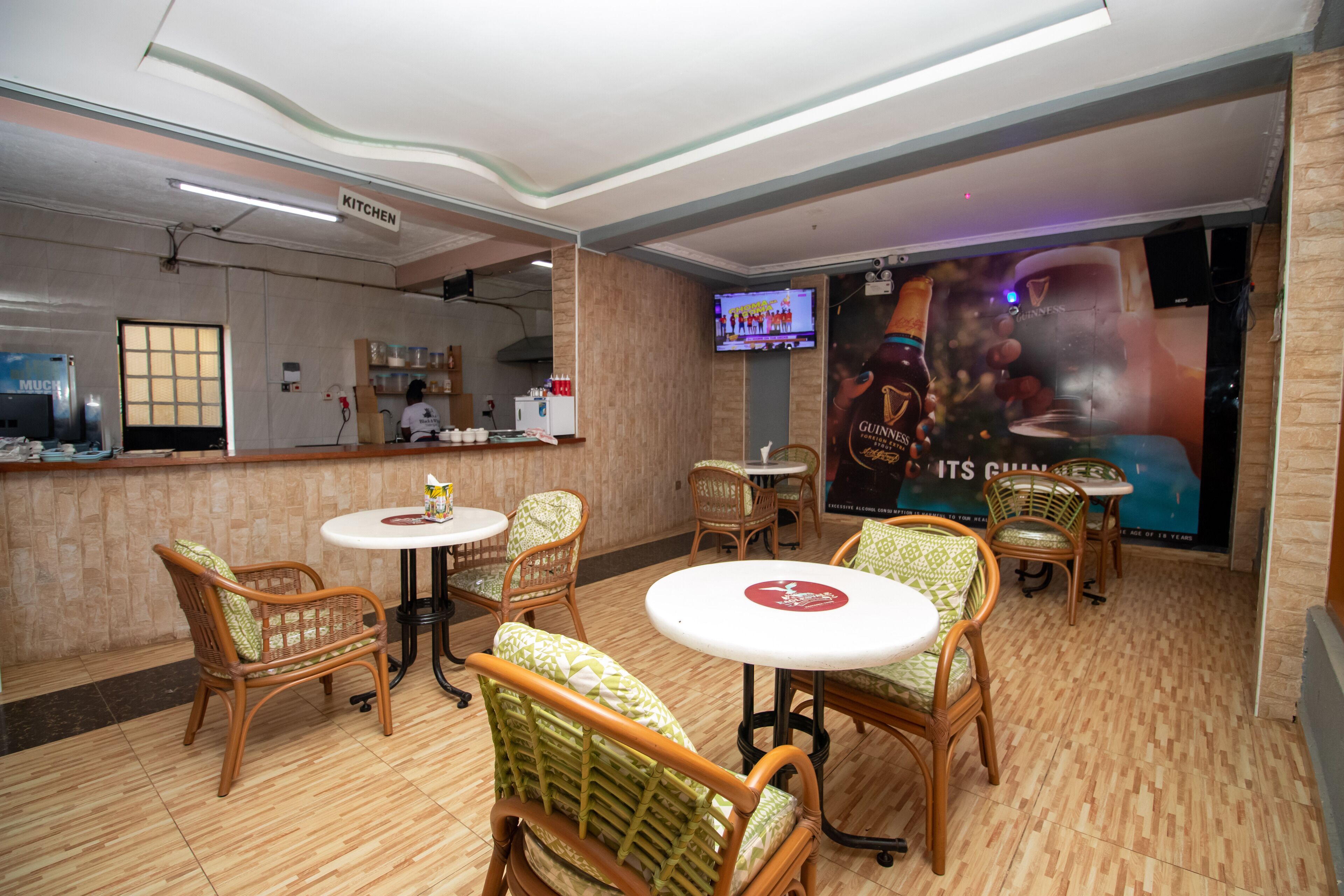 L’intérieur d’un restaurant, avec des chaises en osier, des tables rondes, un espace cuisine et un écran de télévision.