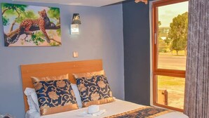 A neatly made bed with a patterned bedspread, a wooden headboard, and a painting of a leopard on the wall. - Eaglesvale Hotel (Naivasha)